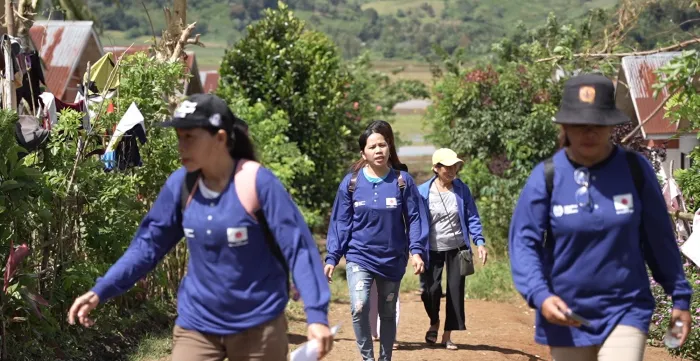 Women in blue shirts walk and visit a community.