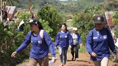Women in blue shirts walk and visit a community.
