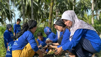 Women plant seeds behind coconut trees